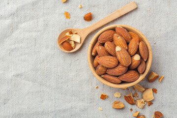 Roasted almonds in wood bowl and spoon on linen table cloth background, top view