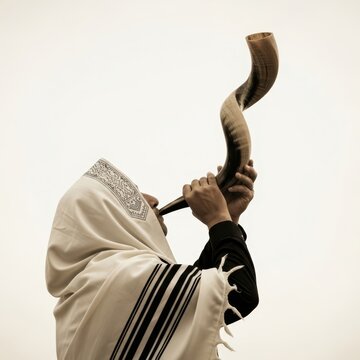A man wrapped in a tallit blowing a shofar on a white background, A man dressed in traditional Jewish attire blows a shofar horn against a plain white backdrop, yom kippur