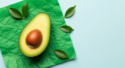 Fresh avocado half with seed and green leaves on green paper background for healthy eating concept