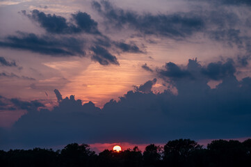 Sunset cloudscape with sun, sky, forest.
