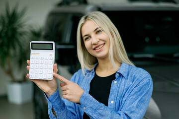 Saleswoman showing calculator and explaining car cost in dealership
