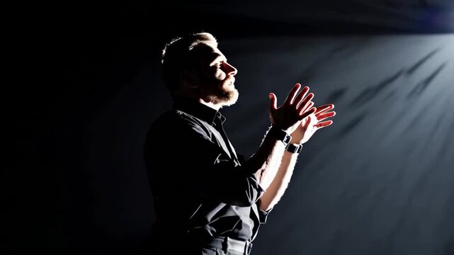 A man is clapping his hands as the light shines on him