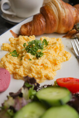 Delicious breakfast plate with scrambled eggs and croissant