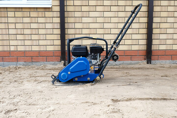 Construction tool - vibrating plate for compacting sand. Preparing the base for a concrete slab.