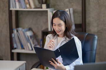 Asian cheerful happy female professional successful doctor practitioner in a white lab coat with a stethoscope standing smiling holding a reading paperwork document in a folder in the hospital.