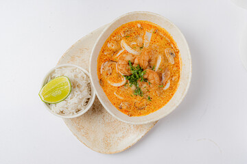 A delicious bowl of shrimp soup filled with aromatic spices, onions, and served with lime and rice