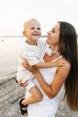 Happy mother holds her three year old son in her arms on the beach