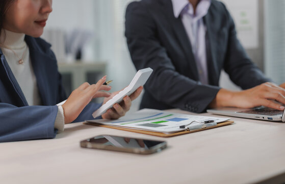 Two business professionals collaborating on financial analysis, using a calculator and laptop, with charts and documents on the desk