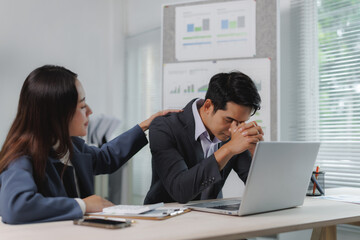 Professional woman comforting male coworker experiencing stress at office desk. Corporate...