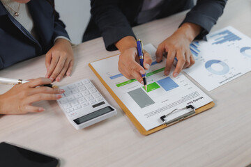 Two business professionals collaborate on financial analysis, using charts and a calculator to make...