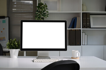 Modern workspace with blank computer screen, potted plant, and coffee mug on a white desk