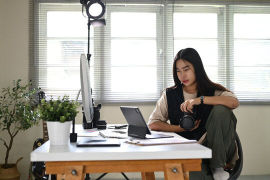 Young female photographer reviewing photos on tablet while, holding a camera
