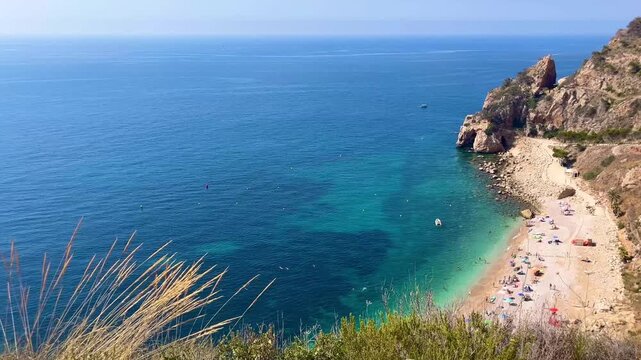 Tourists are swimming and sunbathing at Cala Moraig beach, a beautiful cove with crystal-clear turquoise waters located in Benitachell, Alicante, Spain, during a sunny summer day