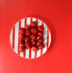 Red ripe strawberries on red striped plate with red background