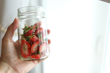 Hand holding clear glass jar of strawberry tops