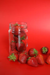 Clear glass jar of healthy organic strawberries on Red