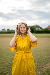 Middle age cheerful woman, wearing yellow dress with headphones
