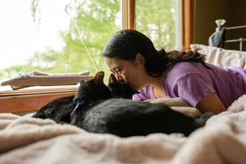Woman with down syndrome kissing black cats on bed