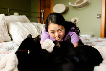 Young woman with down syndrome playing with black cats on bed