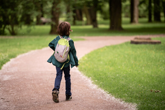 A boy child walking on a park path, carrying a backpack.