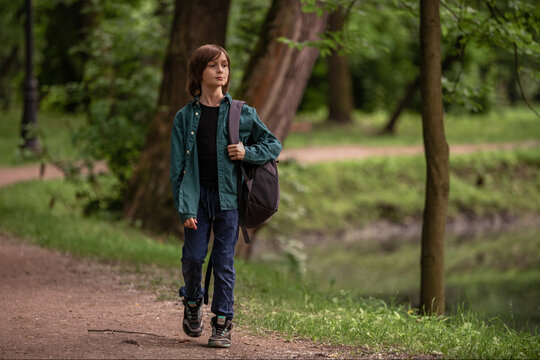 A boy child walking on a park path, carrying a backpack.