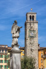 Historic clock tower and statue in Italian town.
