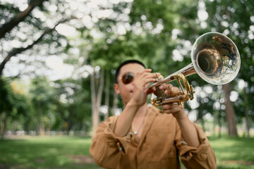 Trumpet player in brown shirt and sunglasses performing in a green forested area