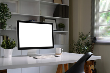 Blank desktop monitor, white desk, coffee mug, and indoor plants in natural light