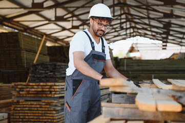 Woodworker picking lumber boards in warehouse, professional wearing hard hat and safety glasses