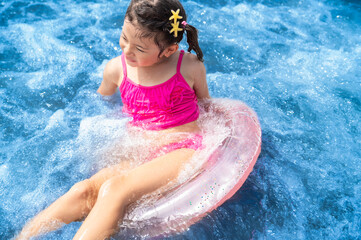 A smiling Japanese girl floats happily in turquoise sea water with a transparent pink inflatable...