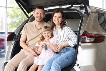 Happy family with keys sitting in car trunk in salon