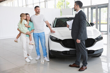 Salesman with clipboard showing new car to happy family in salon