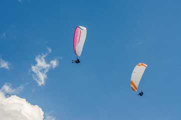 Two colorful paragliders soaring freely against bright blue summer mountain sky. High quality photo