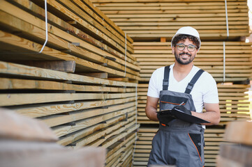 Smiling carpenter holding clipboard, checking lumber inventory in warehouse