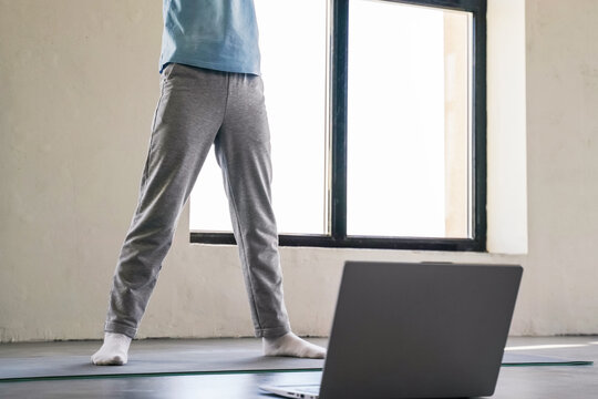 Child practicing yoga at home in front of a laptop during a sunny day
