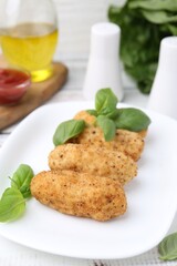 Tasty fried croquettes and basil on white wooden table, closeup