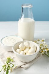 Fresh dairy products and flowers on white wooden table against light blue background