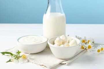 Fresh dairy products and flowers on white wooden table against light blue background, closeup