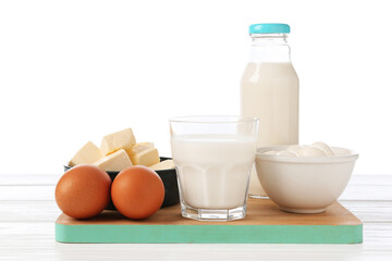 Different dairy products and eggs on wooden table against white background