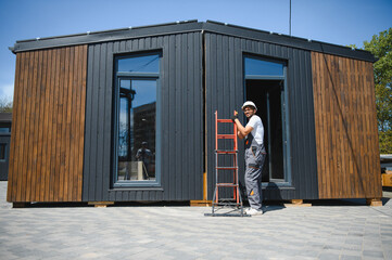 Construction worker moving modular house with ladder