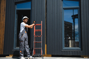 Construction worker moving ladder near modular house