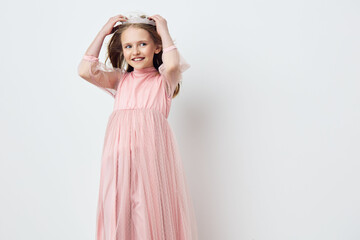Cute girl in a pink dress with a crown, smiling joyfully against a soft white background, ideal for...