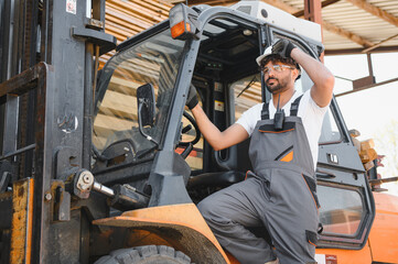 Warehouse worker wearing hardhat and safety glasses driving forklift