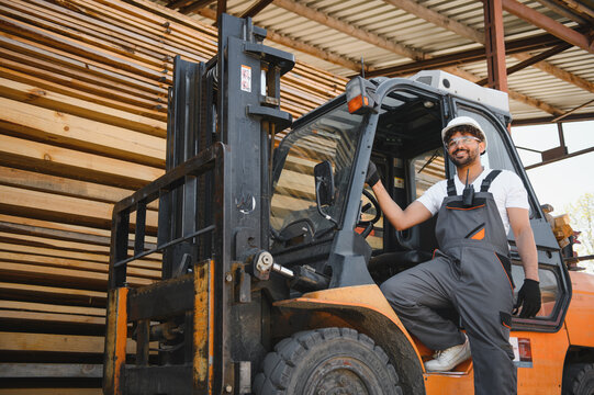 Warehouse worker driving forklift near lumber stacks - Powered by Adobe