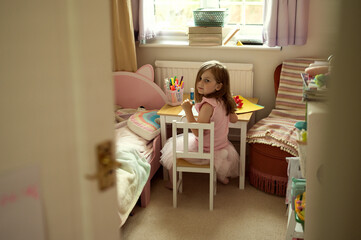 Toddler girl crafting in her room, cutting colorful paper, making card