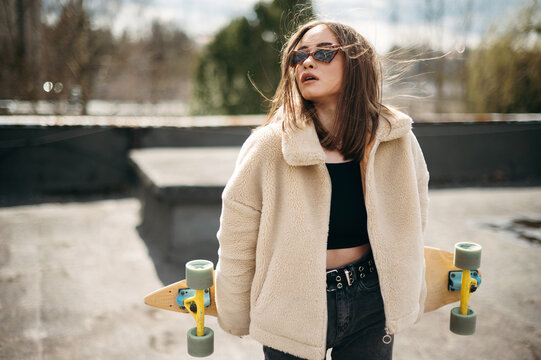 Beautiful woman with skateboard standing on building rooftop