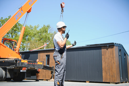 Engineer controlling crane lifting modular house onto truck
