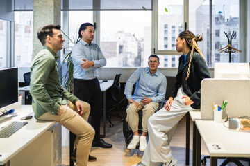 Four young professionals, including a person using a wheelchair, engaging in a productive discussion in a bright, modern coworking office