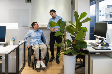 Two young professionals, one using a wheelchair, are discussing work in a bright, modern coworking...
