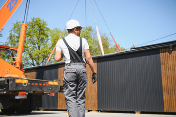 Construction worker supervising lifting of modular house onto truck
